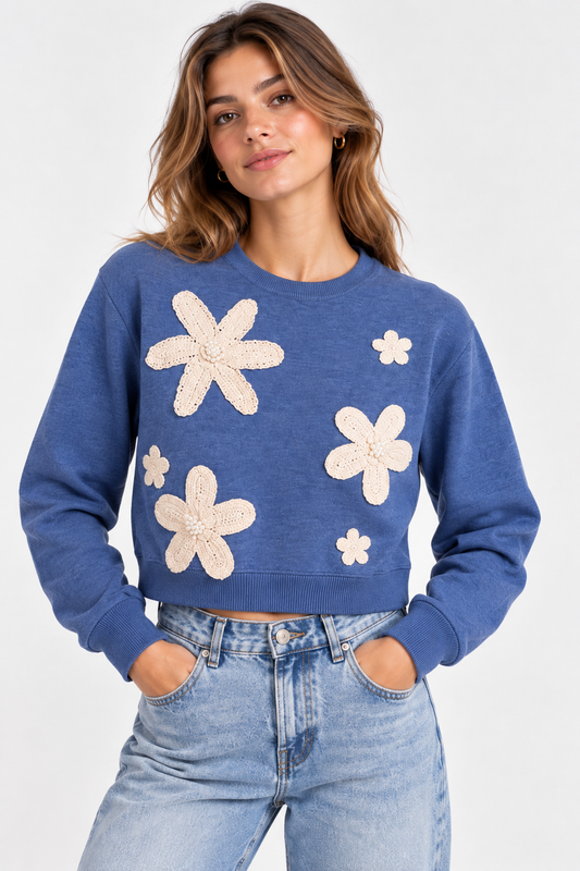 Maglia donna crop azzurra 8090 indossata frontalmente, con girocollo, maniche lunghe e applicazioni floreali color panna con dettagli perlati sul davanti.