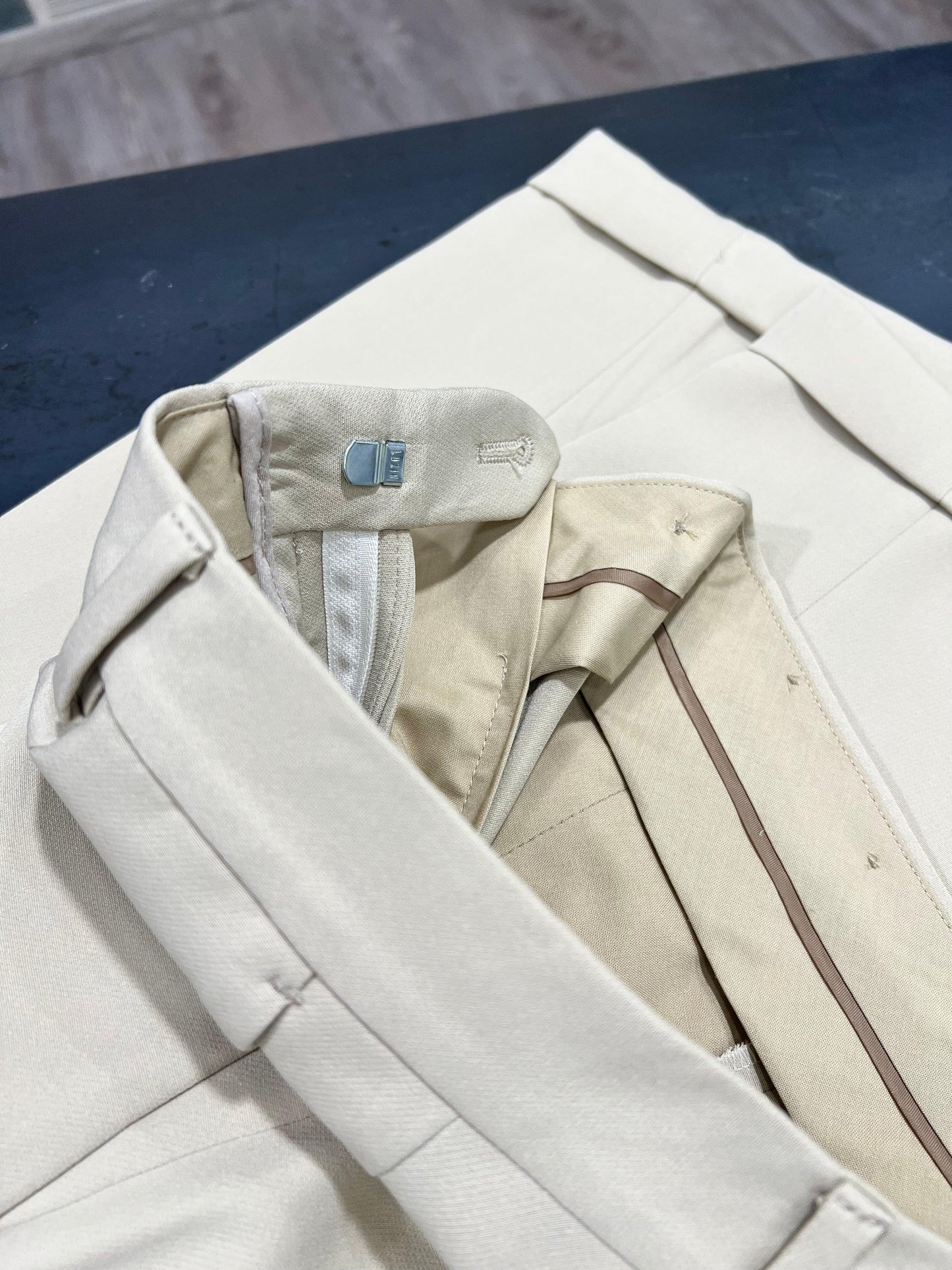 Dettaglio pantalone elegante beige dell'abito uomo doppio petto, tessuto pregiato Made in Italy, chiusura classica.
