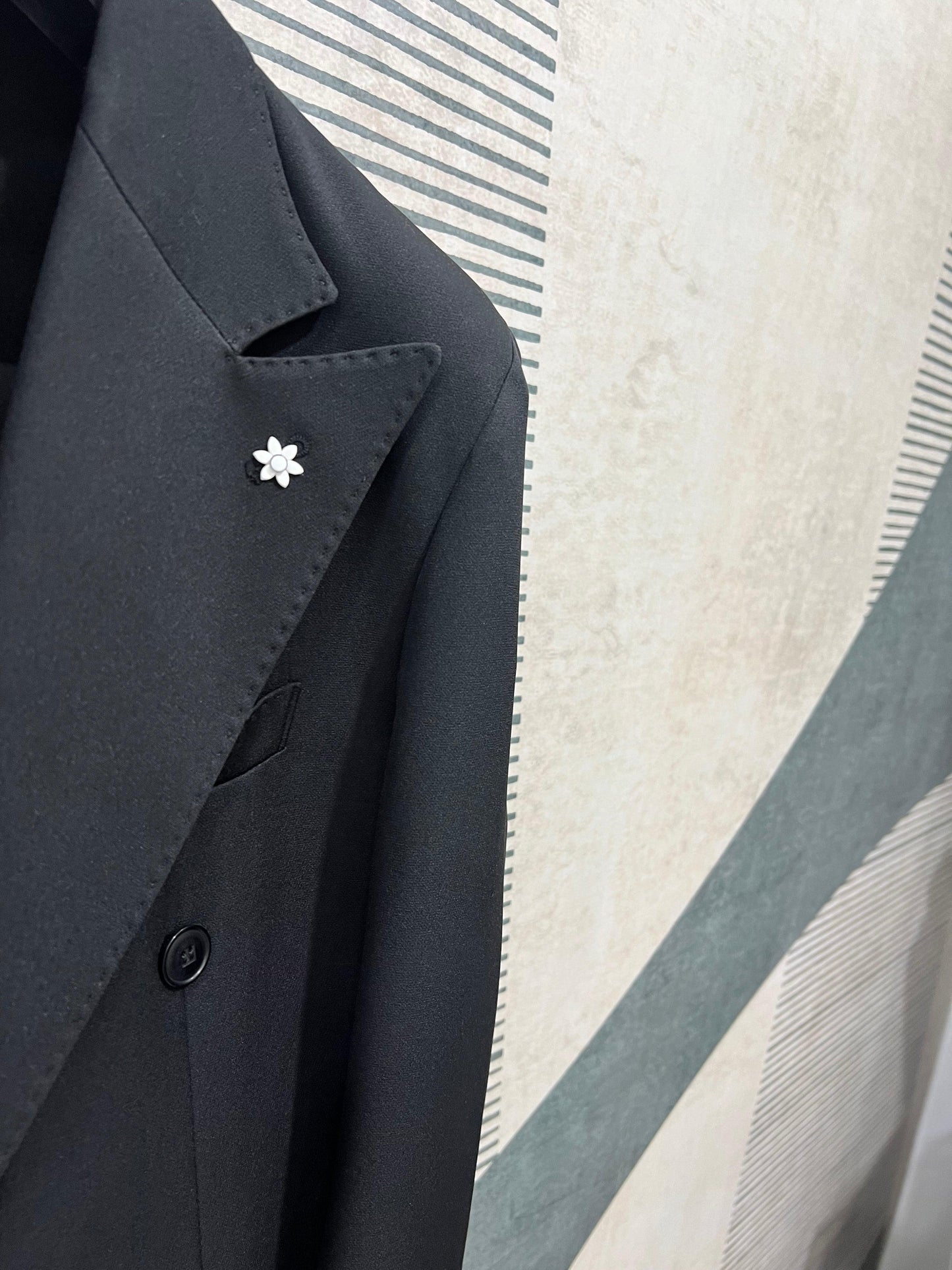 Dettaglio Giacca elegante nera dell'abito uomo doppio petto Made in Italy con spilla fiore su sfondo moderno
