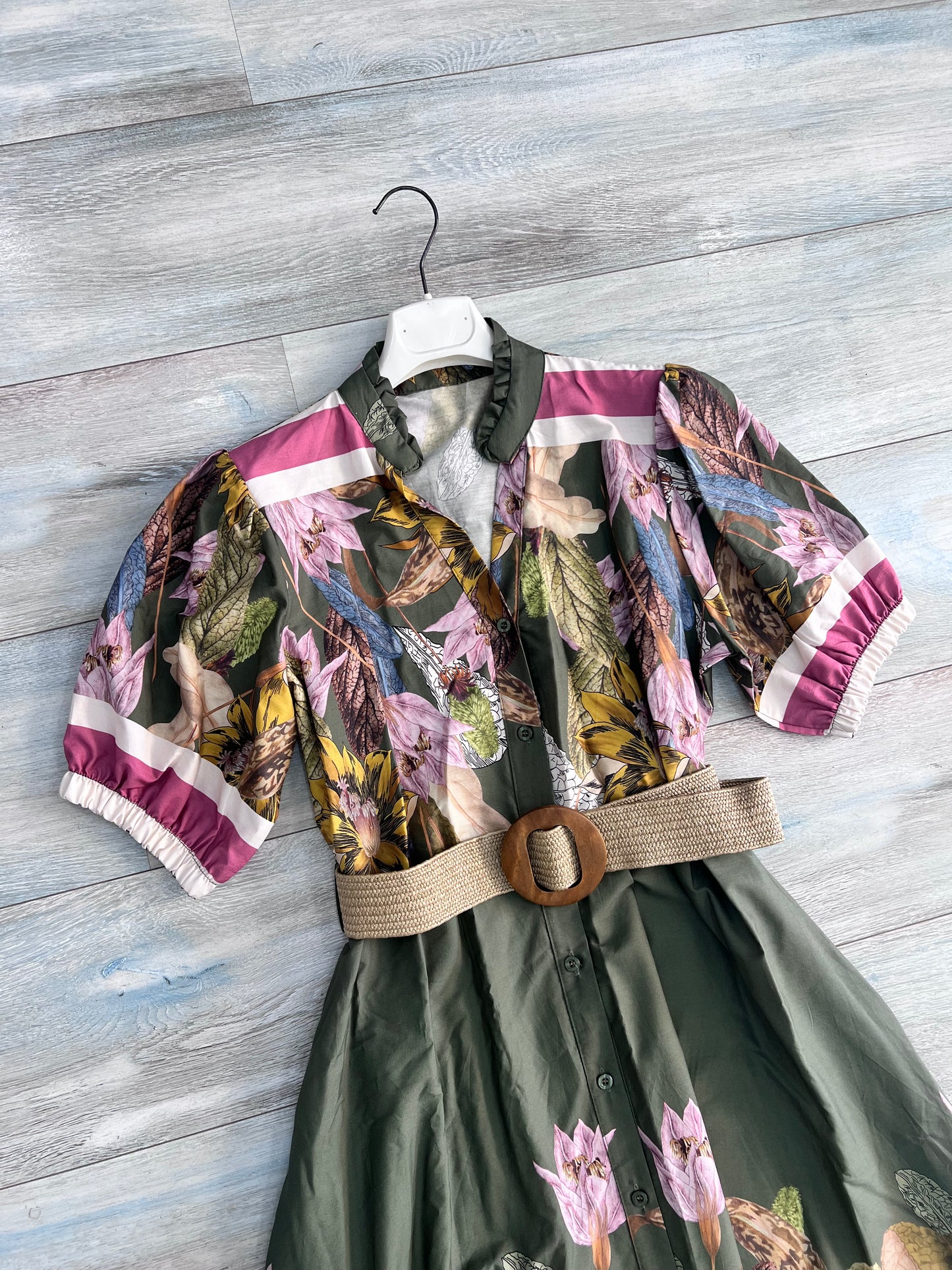 Dettaglio busto abito donna militare: collo coreana con scollo a V, mezza manica con polsino a righe fucsia e elastico arricciato, fantasia botanica con fiori rosa e foglie gialle su fondo verde, cintura in rafia, cotone Made in Italy