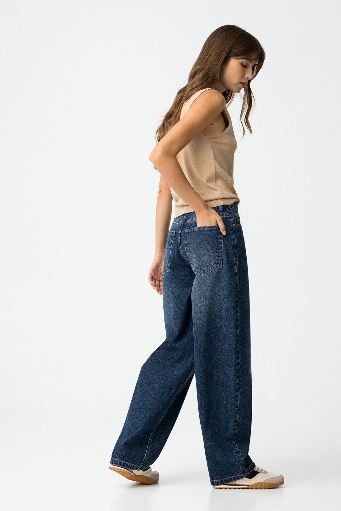 Modella in movimento con jeans balloon vita alta e top beige, vista laterale