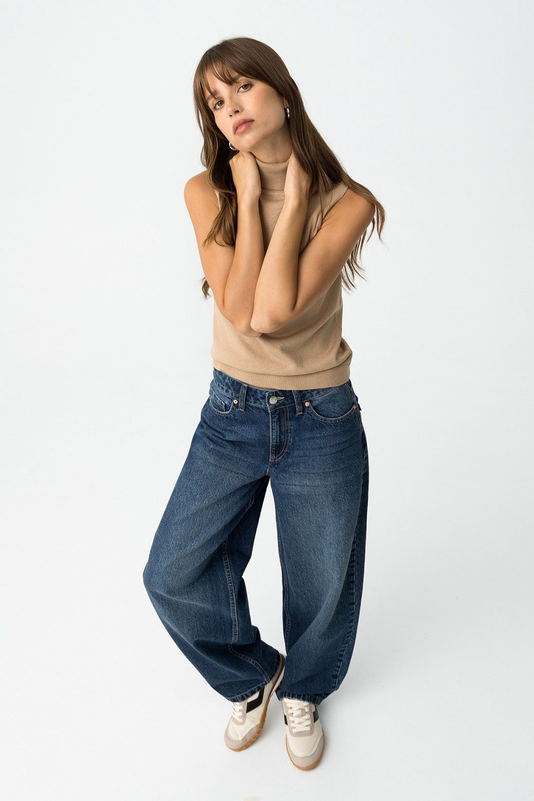 Modella posa frontale con jeans balloon e dolcevita beige, sneakers bianche