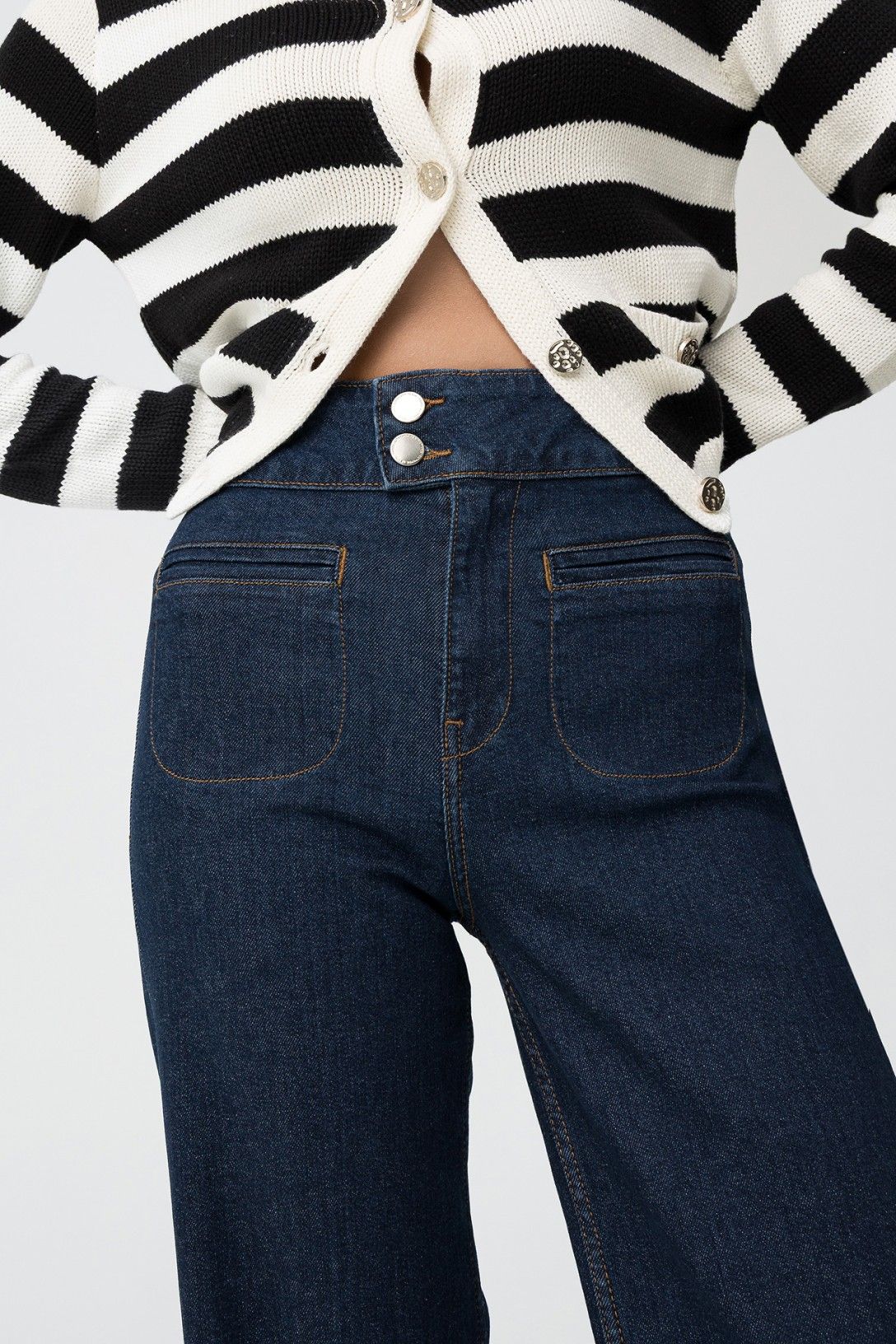 Dettaglio jeans Olivia vita alta con doppio bottone metallico, cardigan a righe aperto, focus su chiusura e tasche frontali