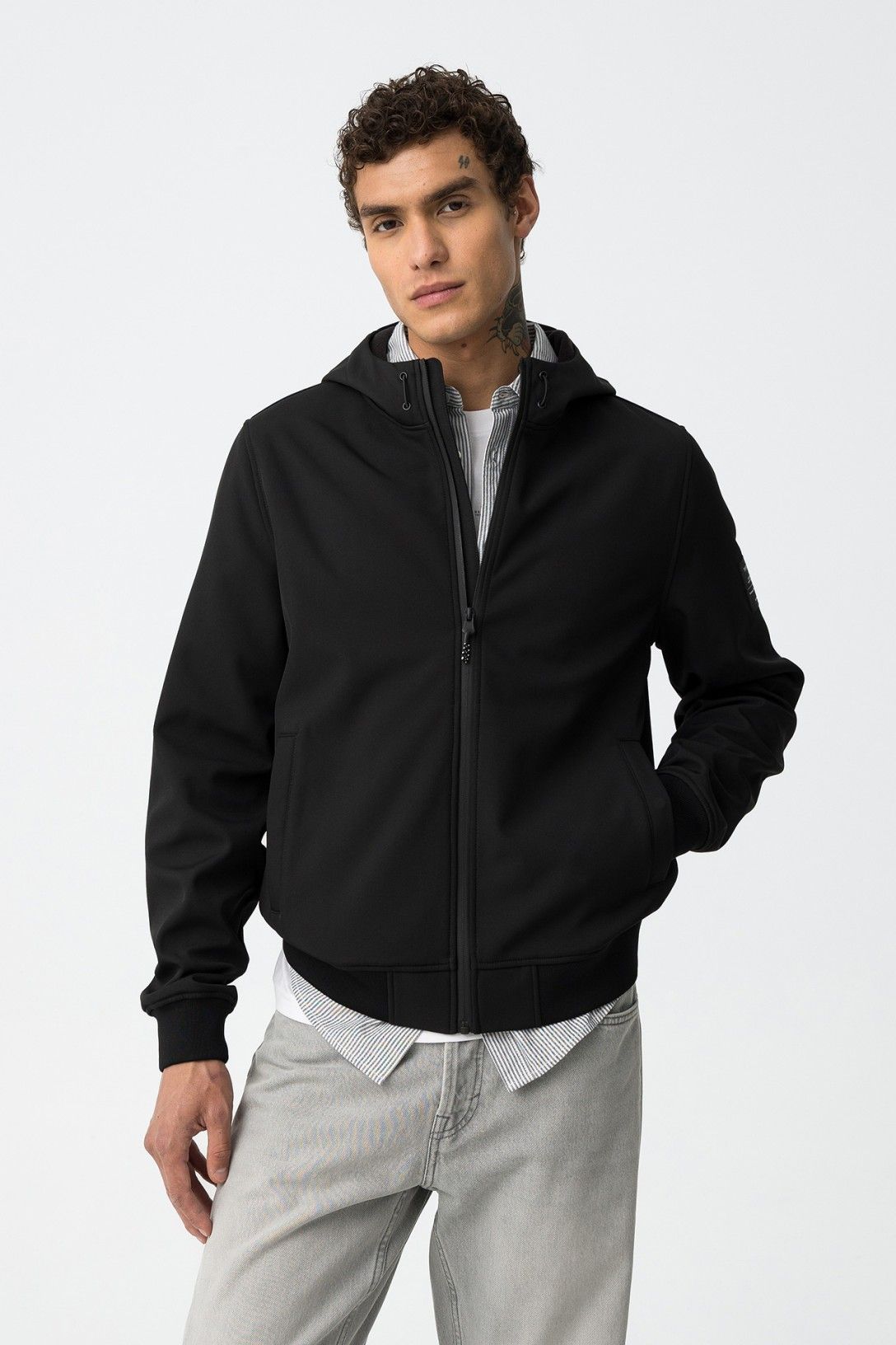 Uomo che indossa giubbotto Pryor nero Tiffosi con cappuccio e zip, abbinato a camicia a righe e jeans grigi