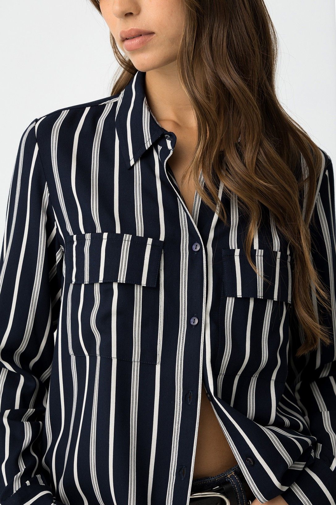 Dettaglio camicia a righe verticali blu navy, tasche frontali con patta e abbottonatura, colletto aperto su jeans