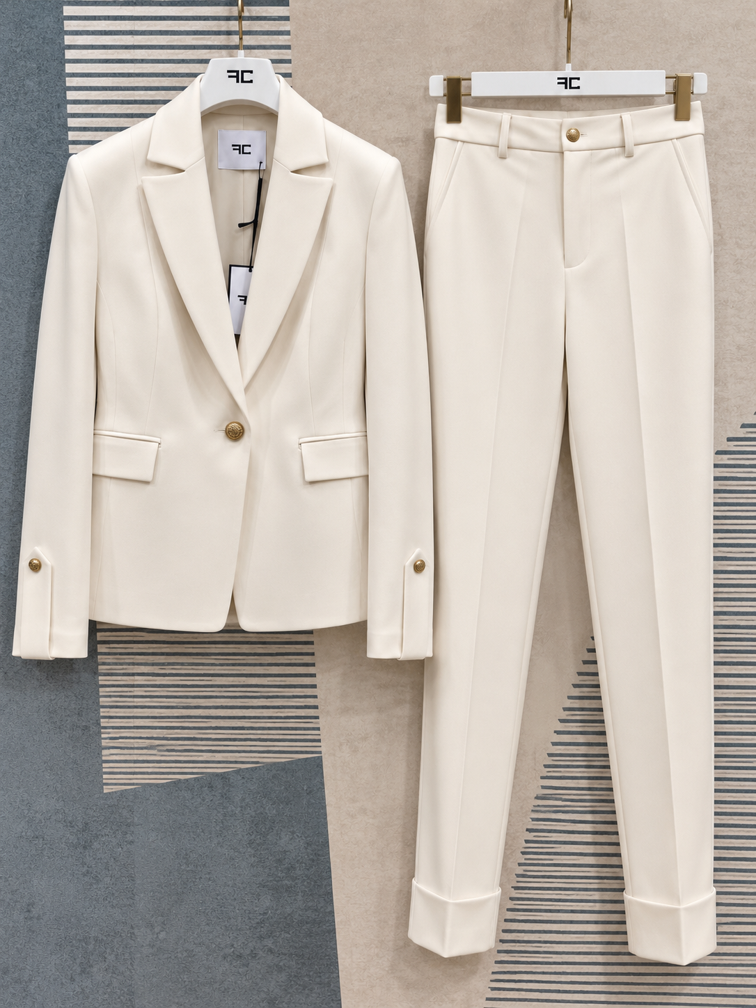 Tailleur donna Aletta panna su grucce, vista frontale della giacca a un bottone e del pantalone coordinato con risvolti.