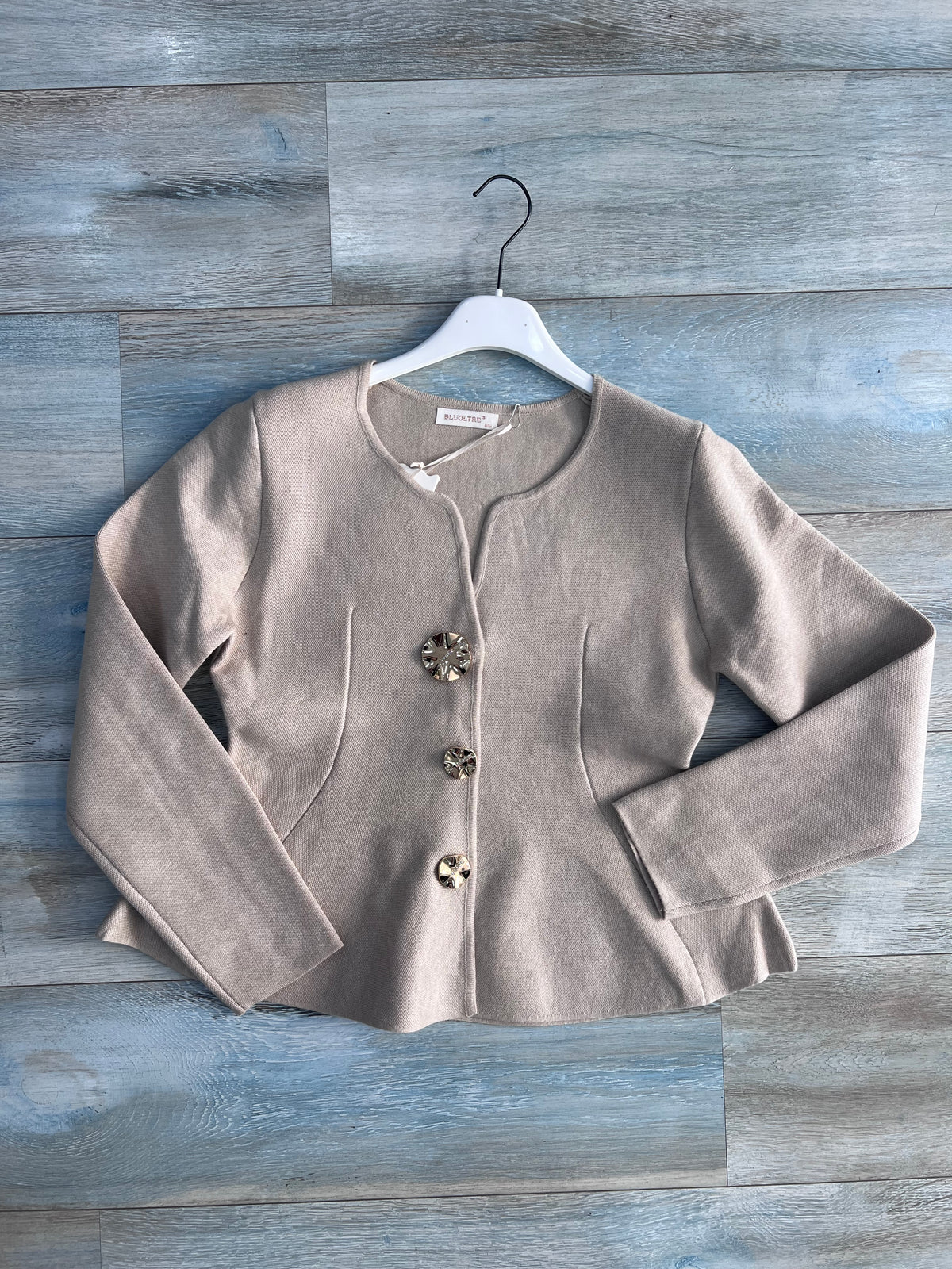 Cardigan donna 872 beige steso su fondo effetto legno, con abbottonatura frontale, tre bottoni gioiello, maniche lunghe e tasche laterali