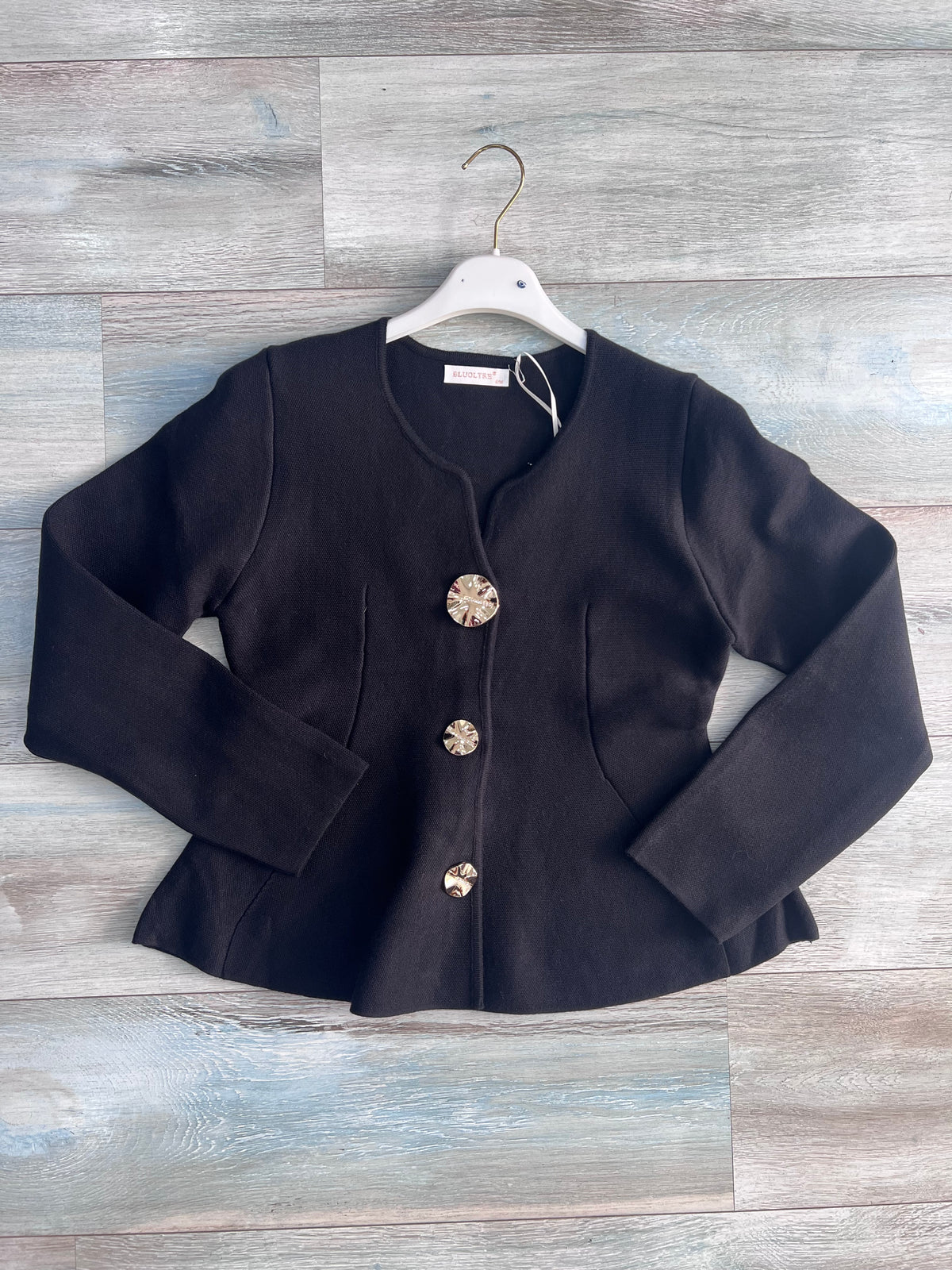 Cardigan donna 872 nero steso su fondo effetto legno, con tre bottoni gioiello, maniche lunghe, tasche laterali e fondo svasato