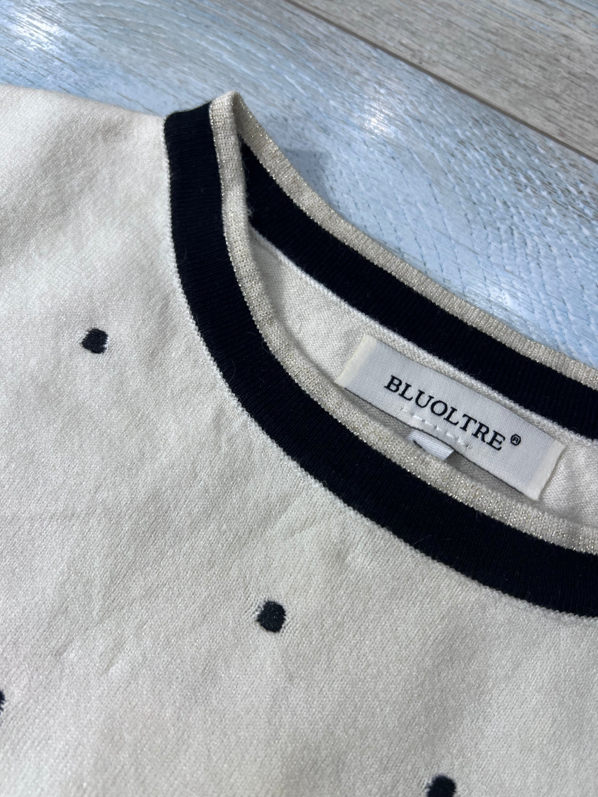 Dettaglio del girocollo della maglia 516 Bluoltre color panna, con bordo nero a contrasto, pois ed etichetta del marchio.