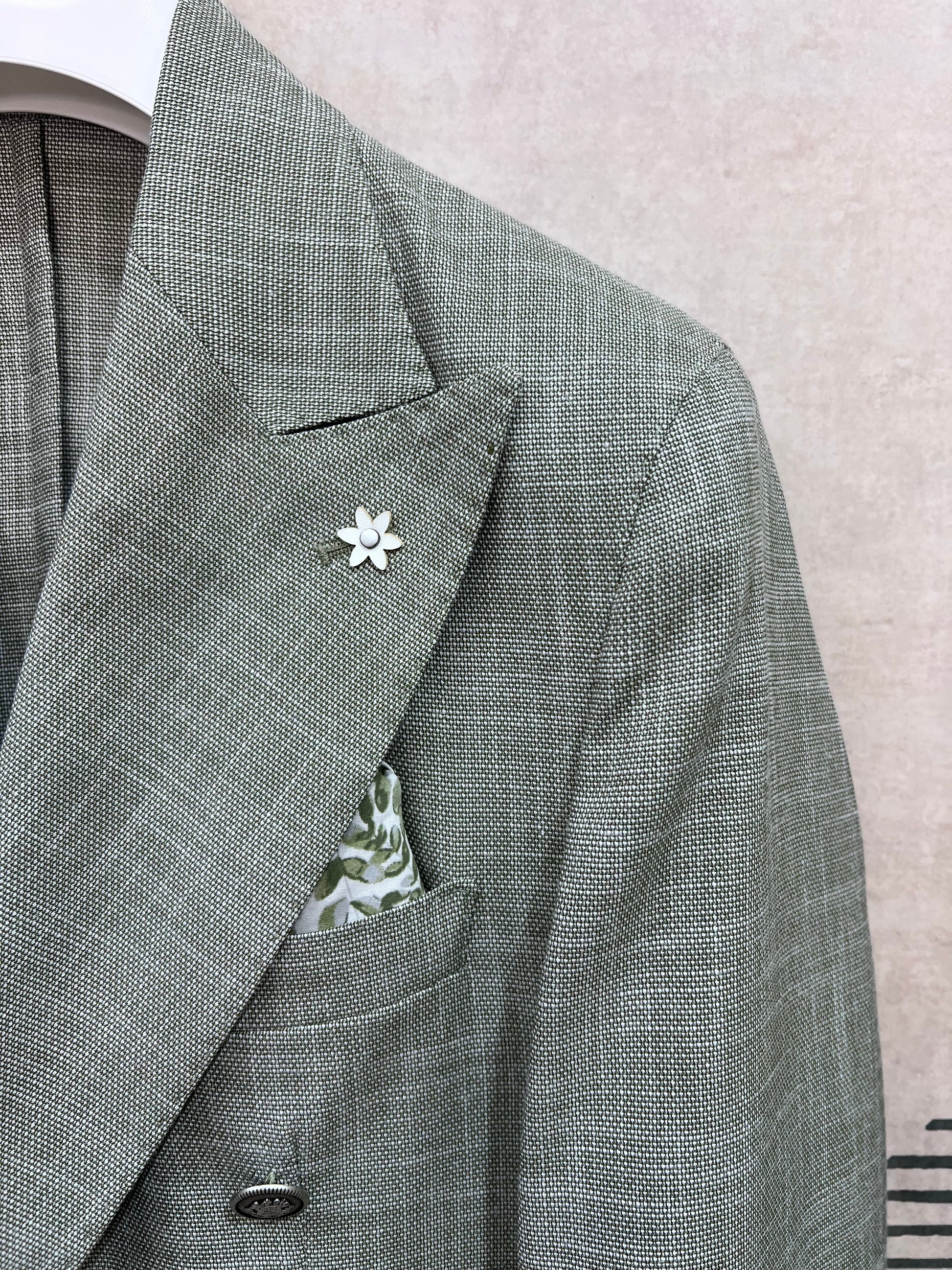 Dettaglio rever giacca doppio petto verde fiammato — trama fiammata effetto lino, spilla fiore bianca e pochette floreale, sartoria Made in Italy dell'abito uomo doppio petto verde