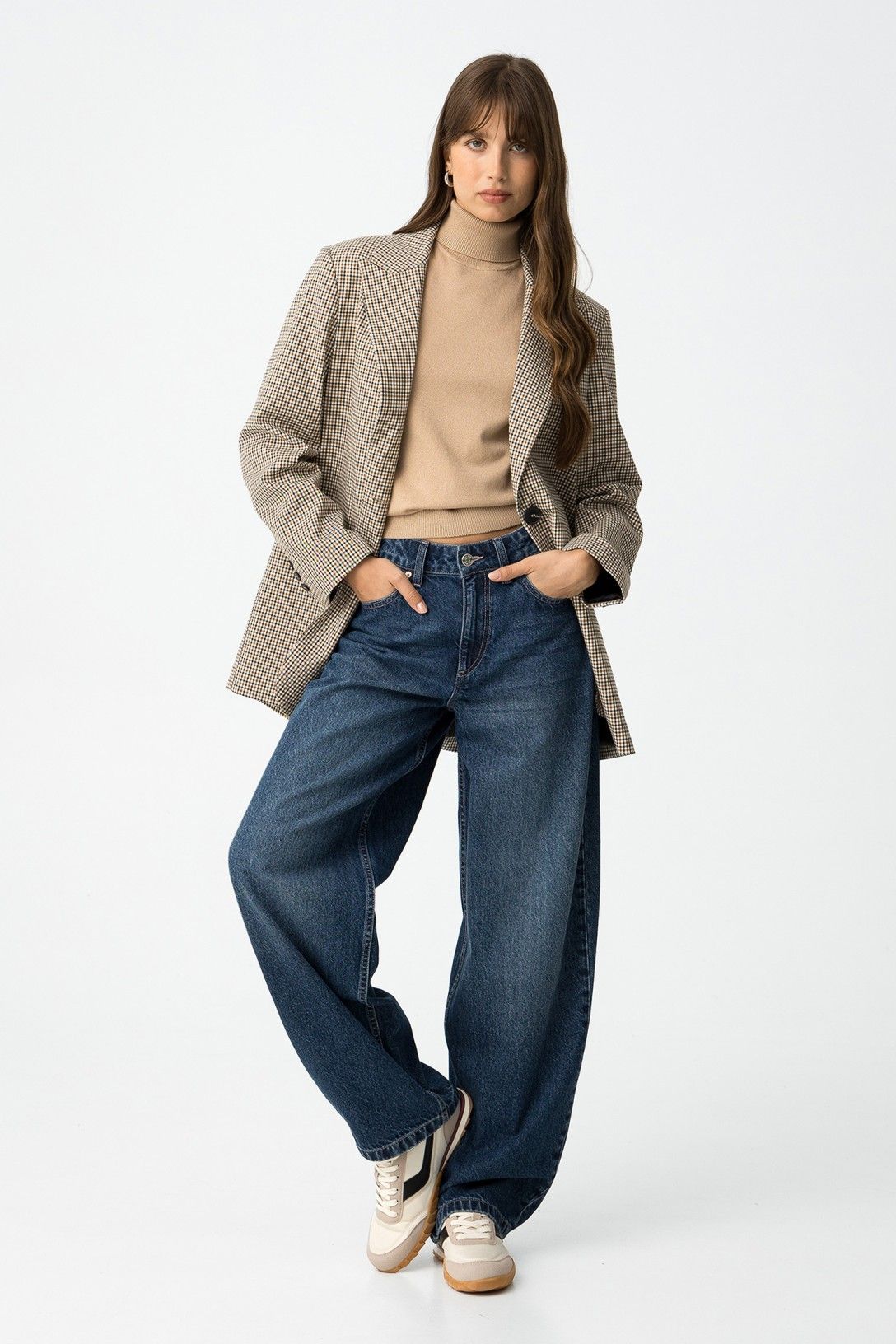 Modella in jeans balloon, dolcevita beige e blazer a quadri con sneakers

