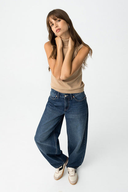 Modella posa frontale con jeans balloon e dolcevita beige, sneakers bianche
