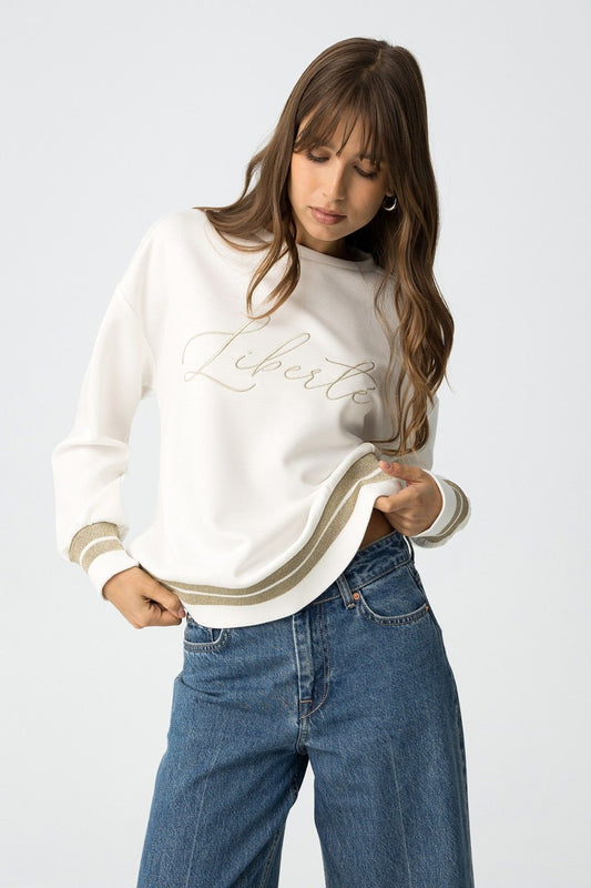 Felpa Gandia bianca con scritta "Liberté" ricamata - modella indossa felpa con jeans blu e finiture dorate
