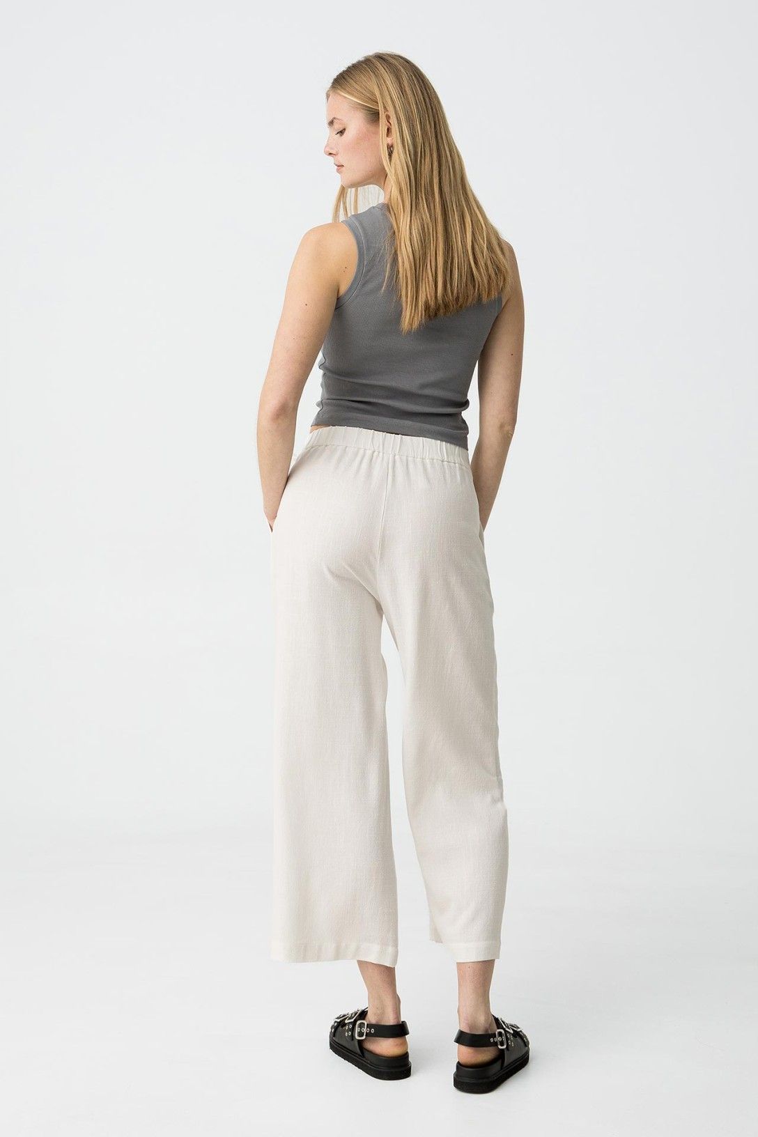 "Pantalone Capri JULIE bianco in lino e viscosa, vista posteriore che mostra la vestibilità ampia e il taglio capri, abbinato a top grigio e sandali"