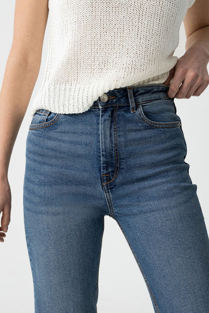 "Dettaglio ravvicinato della vita alta dei jeans Mom_Slim_39 con bottone metallico e zip, indossati con top bianco a maglia"