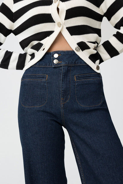 Dettaglio jeans Olivia vita alta con doppio bottone metallico, cardigan a righe aperto, focus su chiusura e tasche frontali
