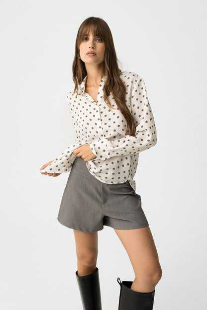Donna che indossa camicia Paradise_3 bianca a pois grigi, abbinata a shorts grigi e stivali neri - look completo