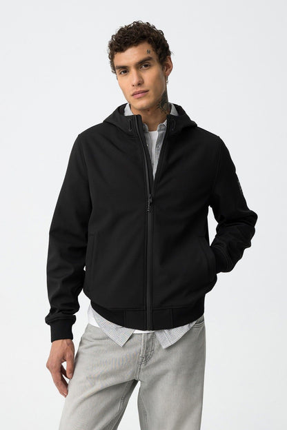 Uomo che indossa giubbotto Pryor nero Tiffosi con cappuccio e zip, abbinato a camicia a righe e jeans grigi

