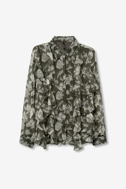 Camicia Quimbe_1 Tiffosi stesa su sfondo neutro, stampa botanica all-over su tessuto semitrasparente, colletto classico e volant decorativi
