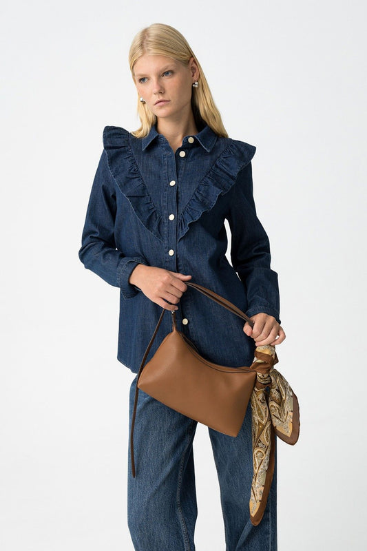 Donna indossa camicia denim West con volant e jeans, tiene borsa cognac
