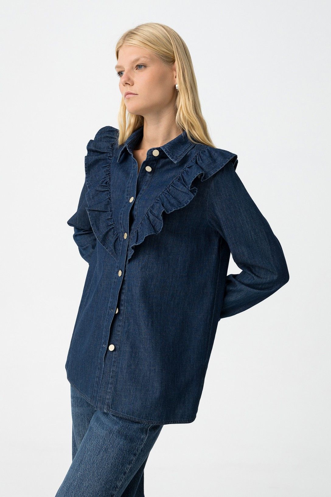 Modella indossa camicia denim West con volant, pose laterale su sfondo bianco
