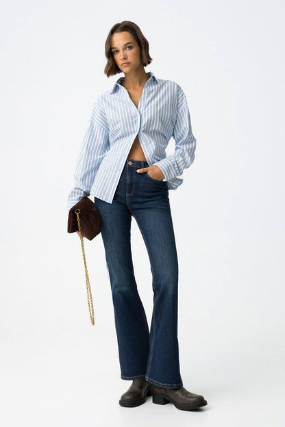Jeans donna blu denim flare vita alta modello Zoe 64 Frarò, vista frontale su modella con camicia a righe azzurra aperta, borsa a tracolla marrone e stivali Chelsea
