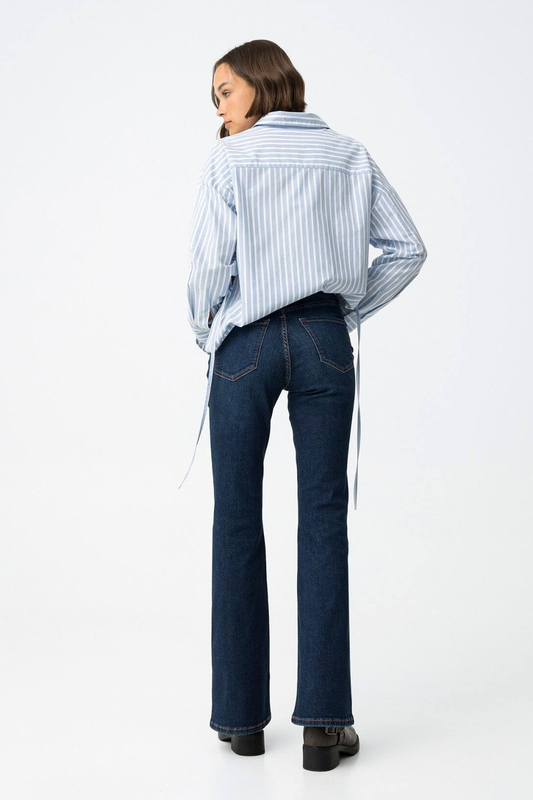 Vista posteriore jeans donna blu denim flare vita alta Zoe 64 Frarò, tasche posteriori e silhouette a zampa, modella con camicia a righe azzurra e stivali biker neri
