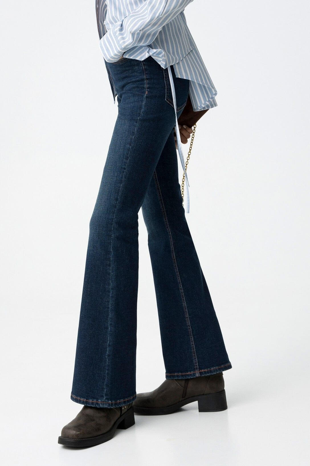 Jeans donna blu denim flare vita alta Amy Zoe 64 Frarò, vista laterale su modella con camicia a righe azzurra annodata e stivali biker neri con fibbia, gamba a zampa in evidenza
