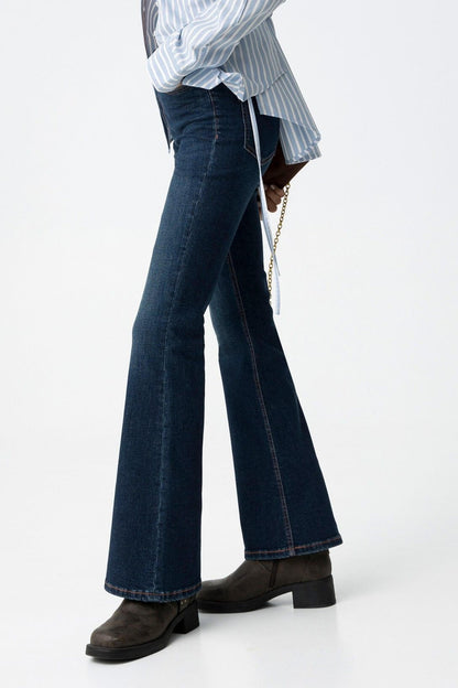 Jeans donna blu denim flare vita alta Amy Zoe 64 Frarò, vista laterale su modella con camicia a righe azzurra annodata e stivali biker neri con fibbia, gamba a zampa in evidenza
